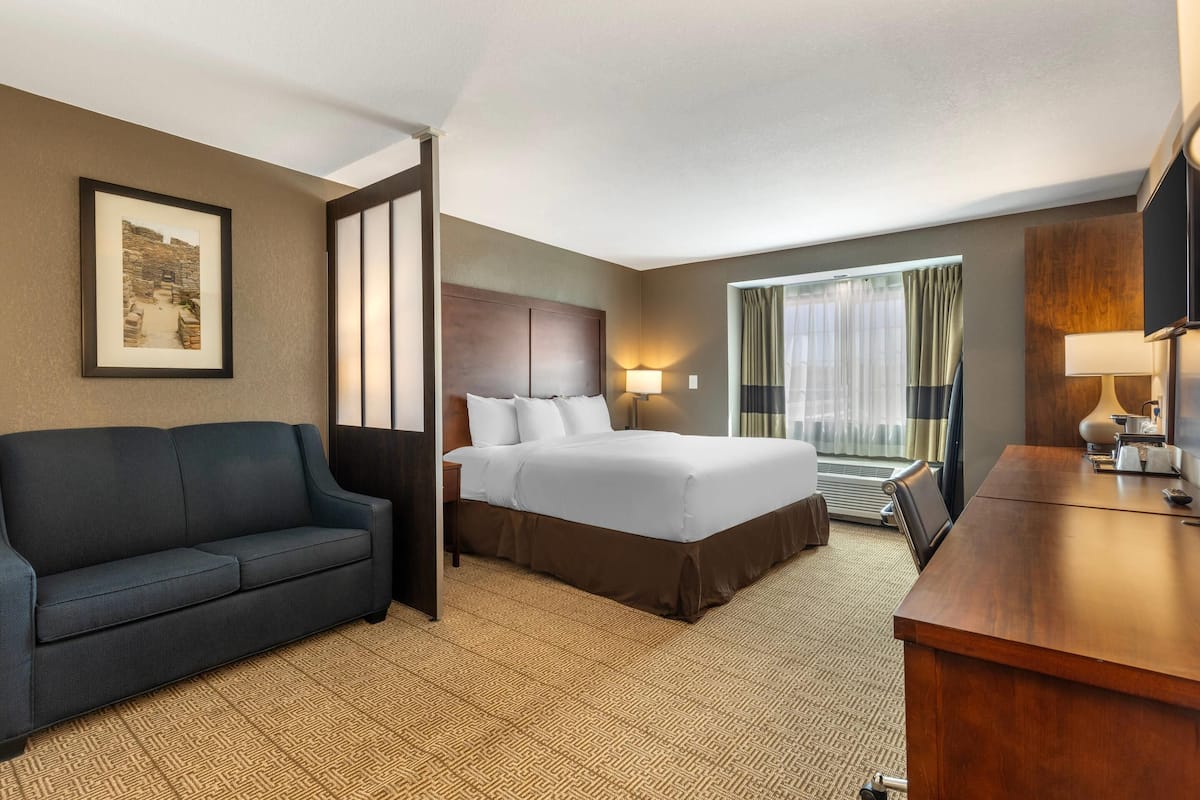 Una habitación de hotel con cama, sofá, escritorio y un ventanal con cortinas.