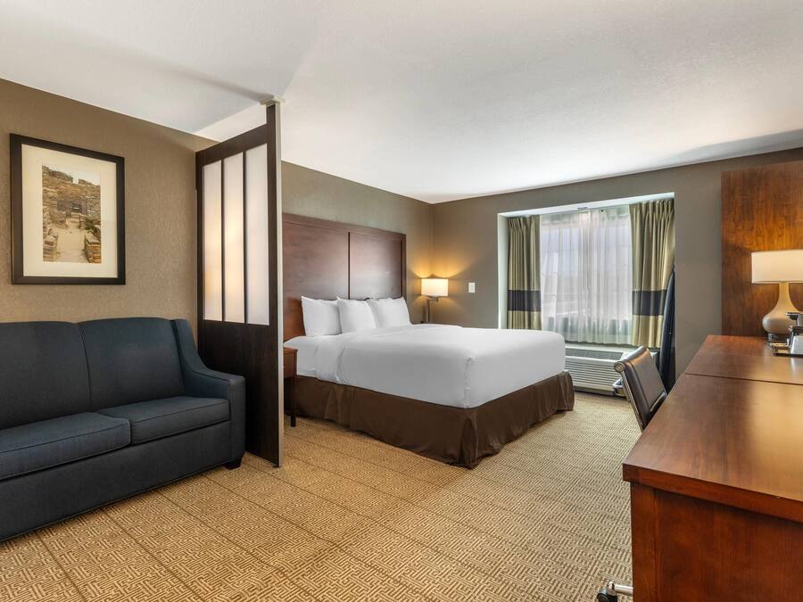 A hotel room with a bed, a sofa, a desk, and a large window with curtains.