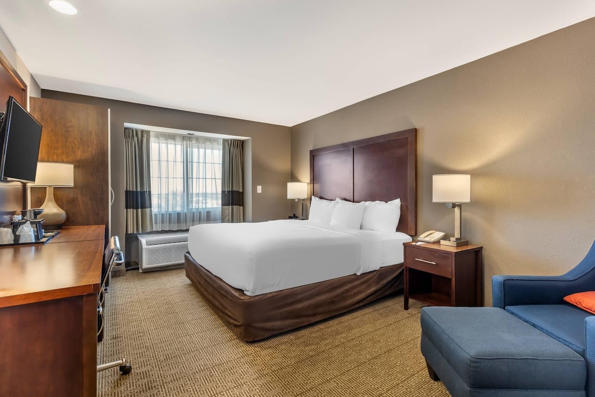Una habitación de hotel con una cama grande, mesitas de noche, un escritorio con computadora y televisión.