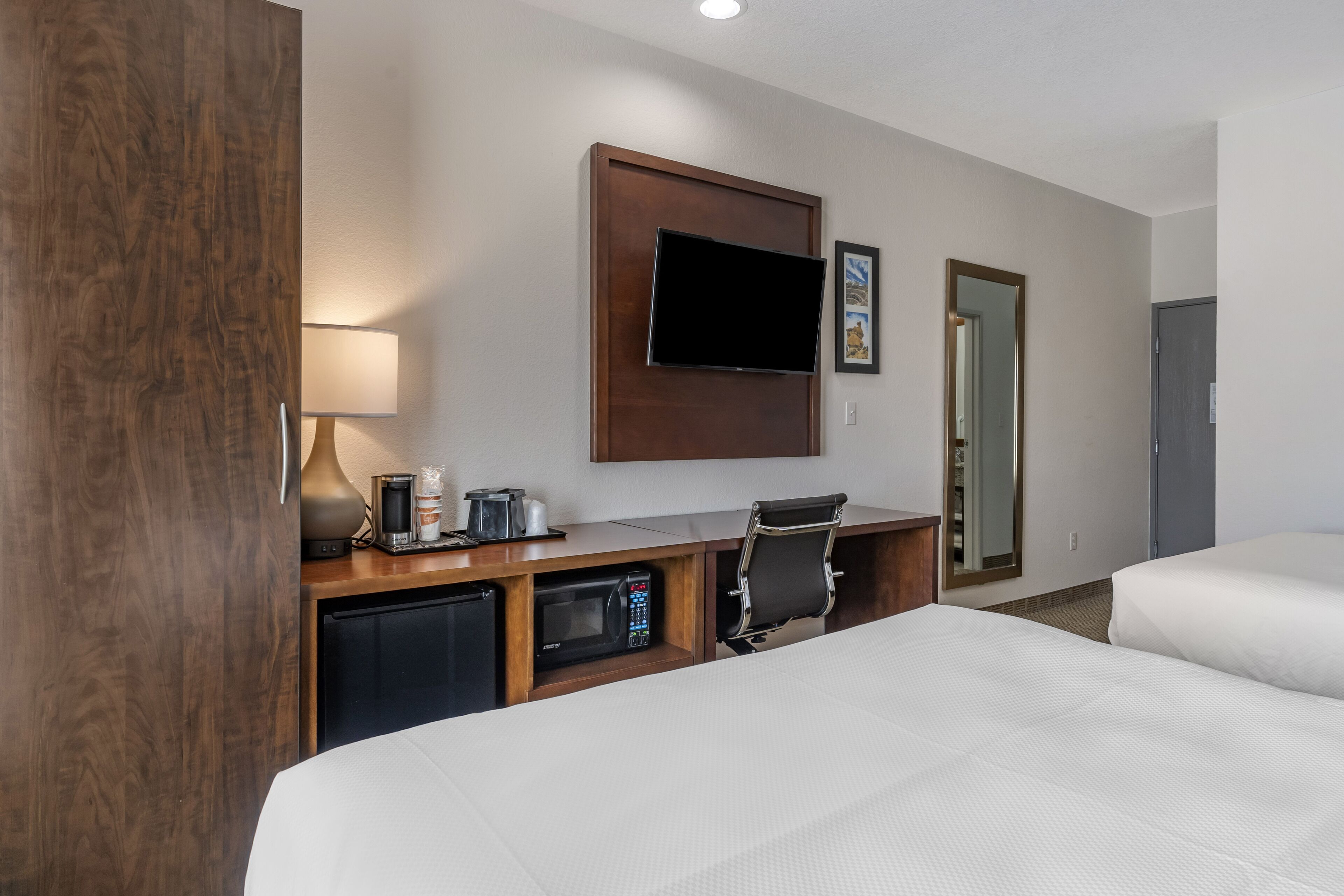 A hotel room with a bed, a desk with a computer, a TV, a microwave, and a coffee maker.