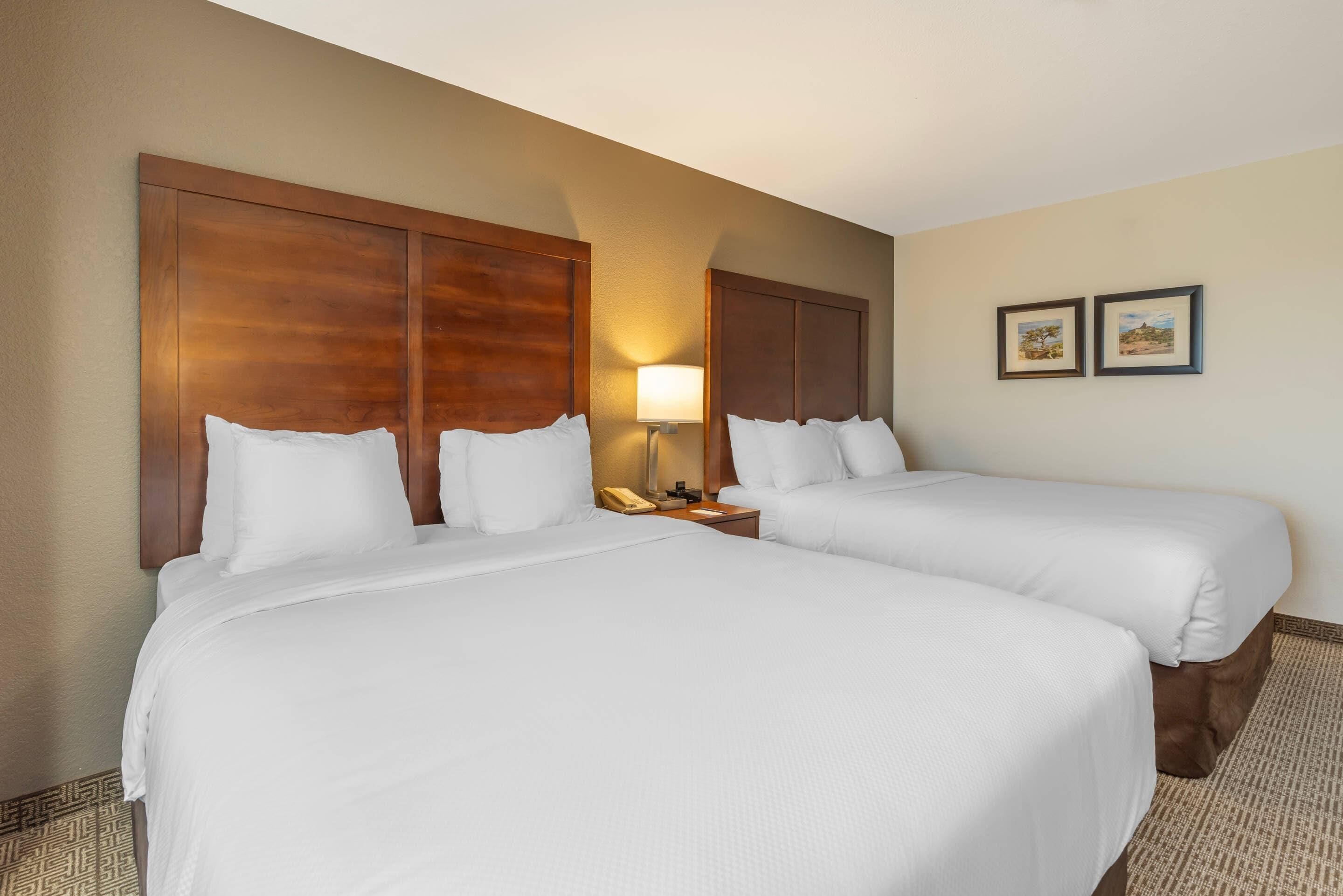 A hotel room with two beds, a nightstand with a lamp, and two framed pictures on the wall.