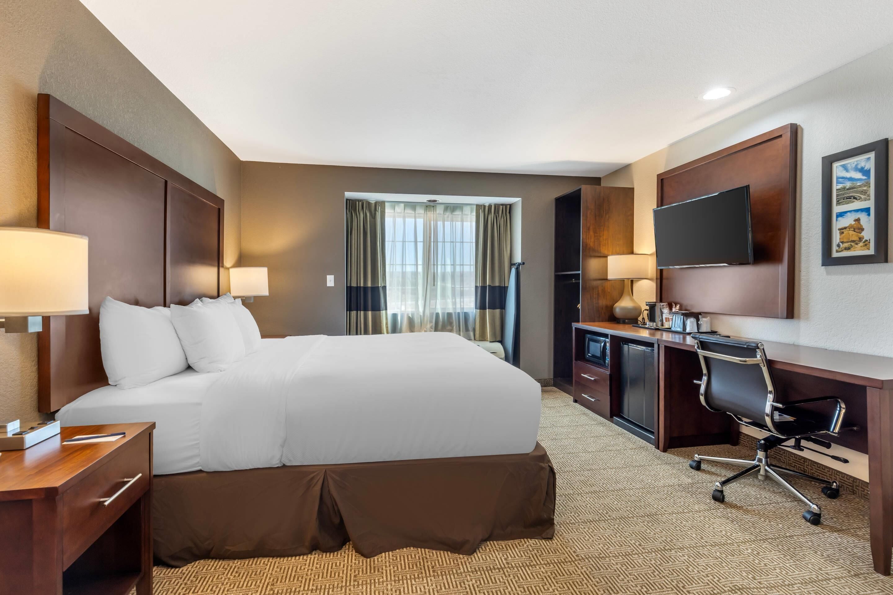 Una habitación de hotel con una cama grande, un escritorio con silla, un televisor y una ventana con cortinas.