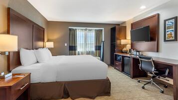 Una habitación de hotel con una cama grande, un escritorio con silla, un televisor y una ventana con cortinas.