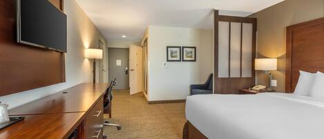 Habitación de hotel con una cama grande, un escritorio con televisor de pantalla plana, una silla y una mesita de noche con lámpara.