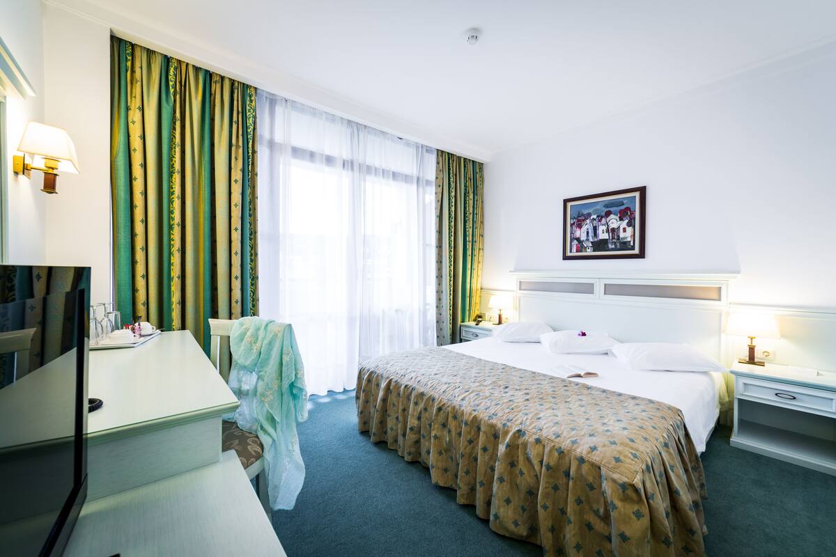 A hotel room with a bed, bedside tables, a desk, a chair, and a television.