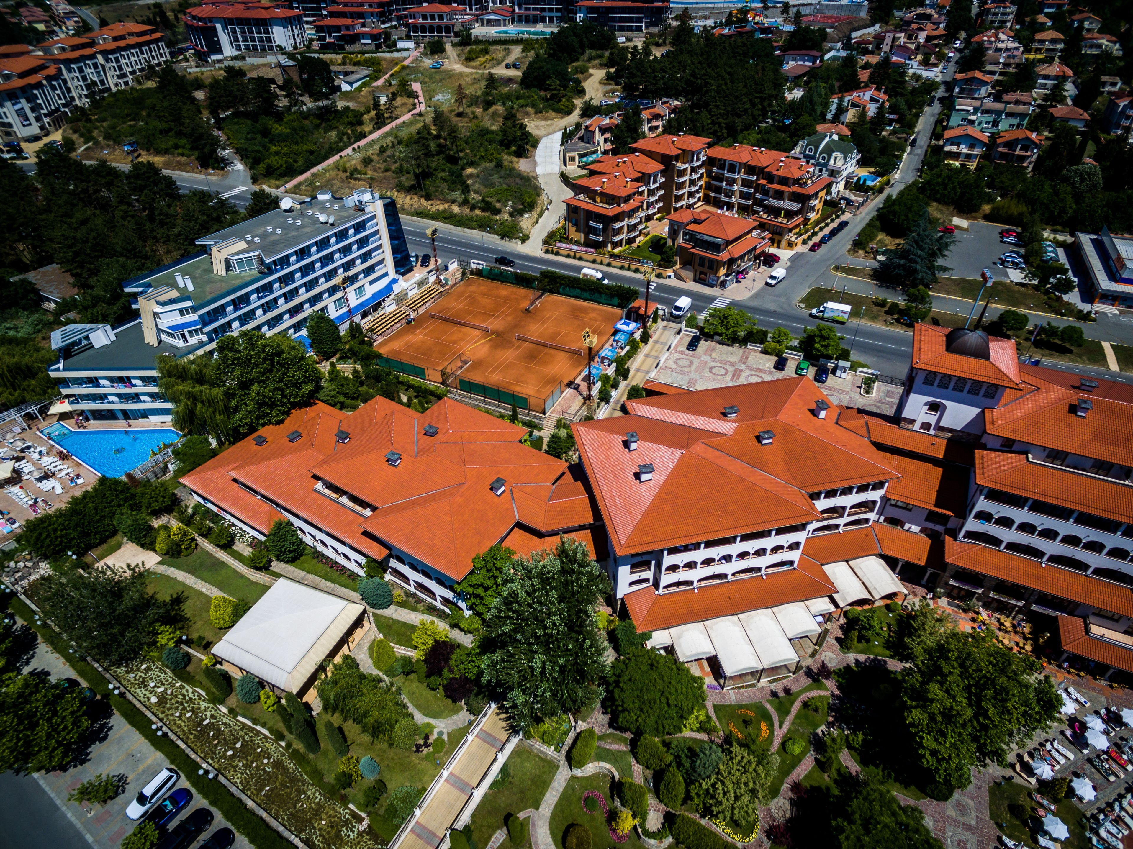 An aerial view of a residential area with multiple buildings, including a large complex with a swimming pool and several smaller houses with red roofs.