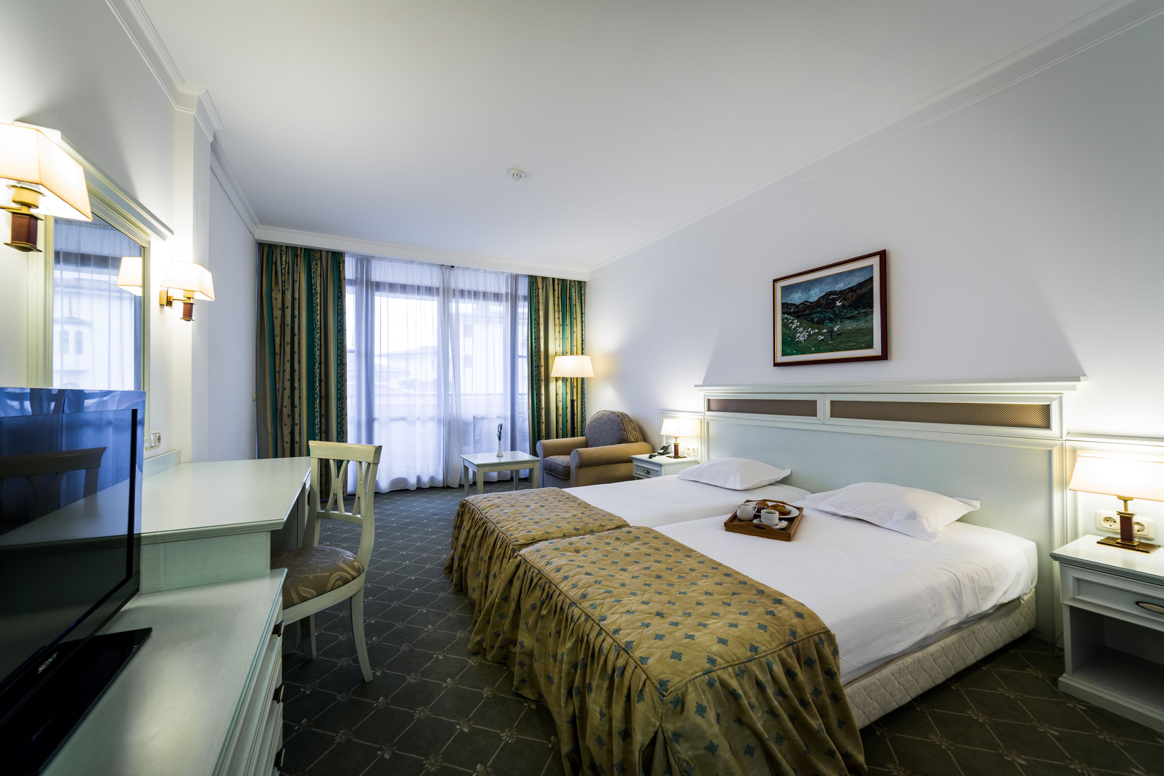 Ein Hotelzimmer mit einem Bett, zwei Nachttischen, einem Schreibtisch mit Stuhl, einem Fernseher und einem Fenster mit Vorhängen.
