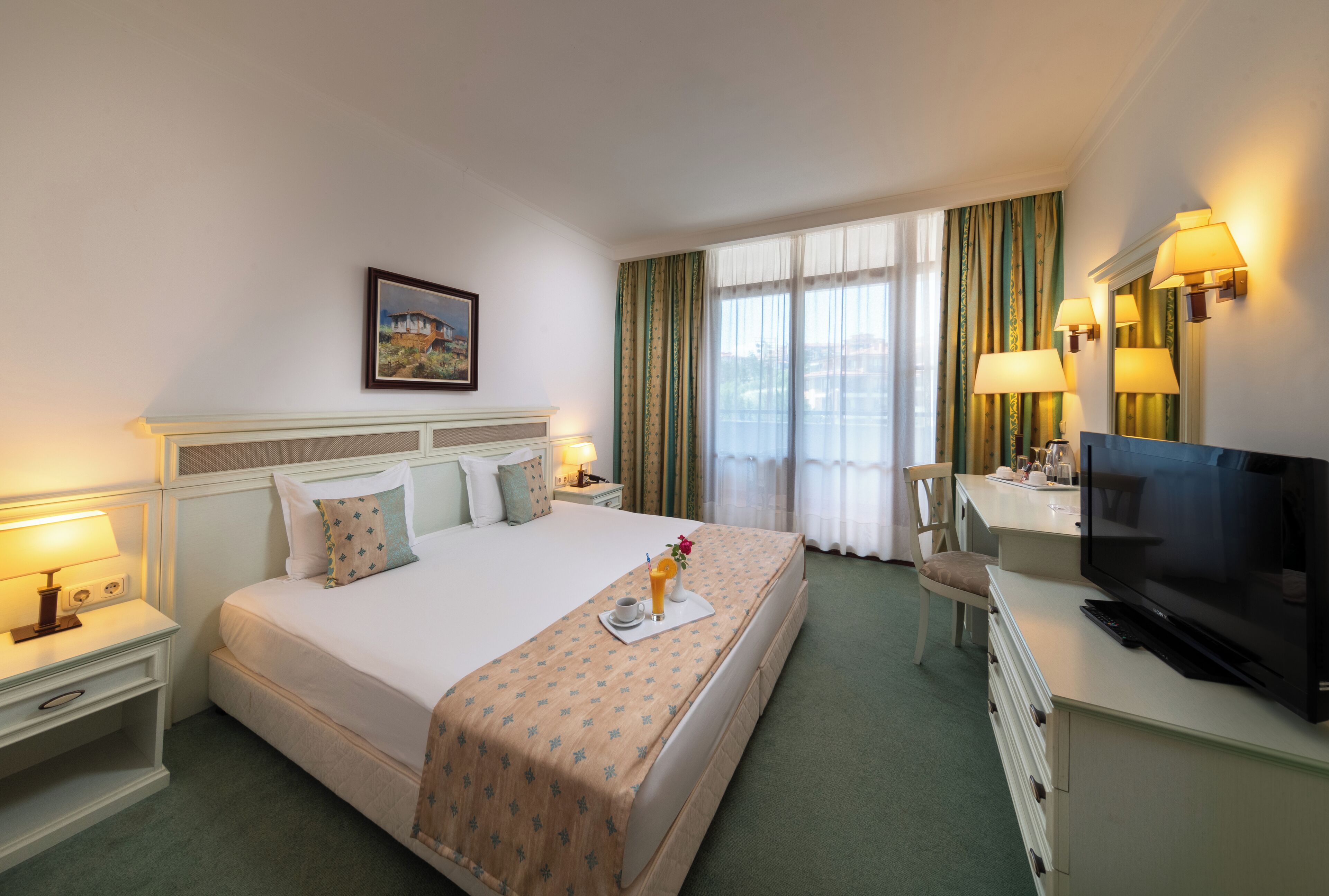 Una habitación de hotel con cama, escritorio con televisor, silla y ventana con cortinas.