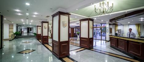 A hotel reception area with a polished floor, a reception desk, and a chandelier.
