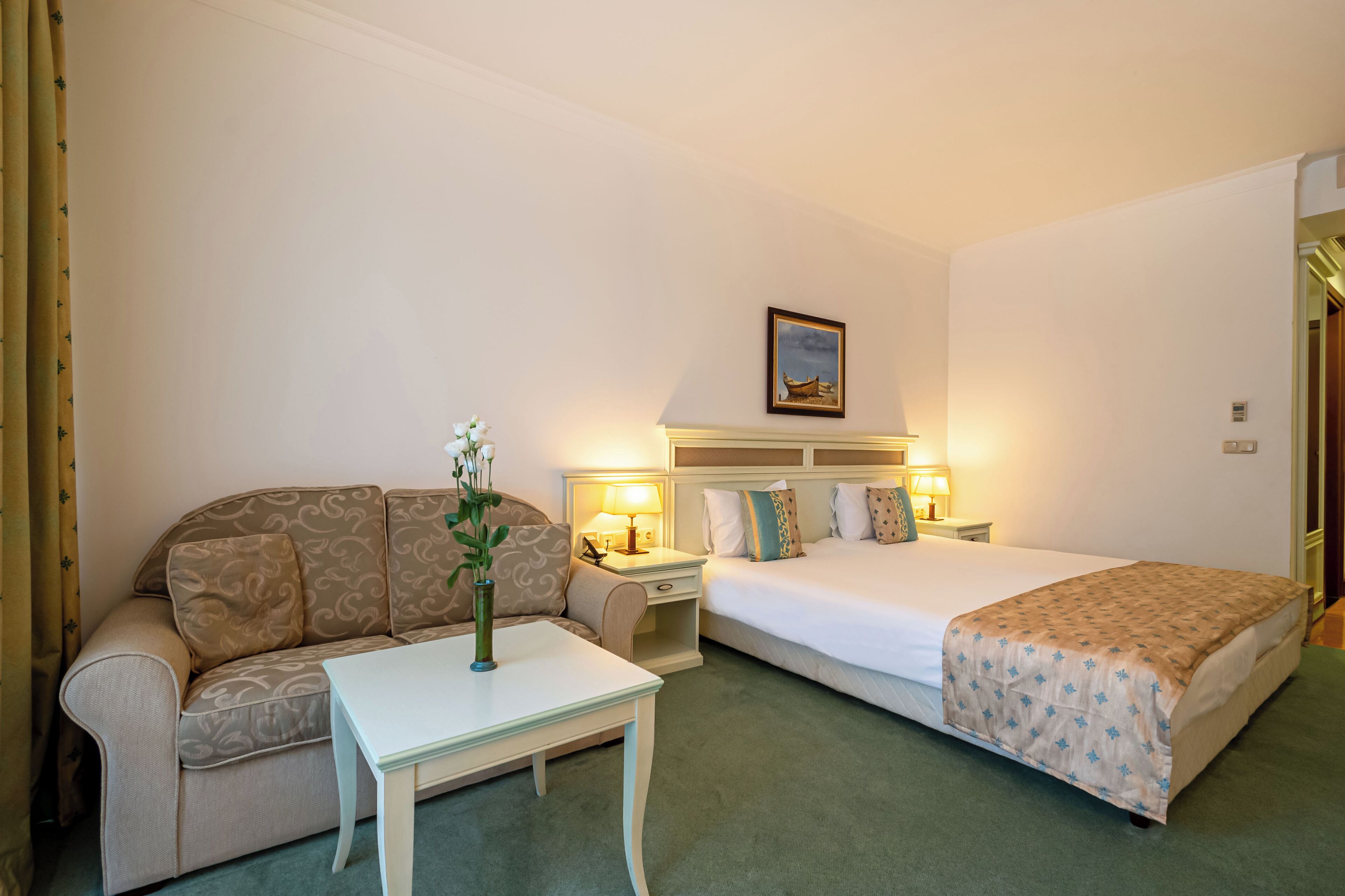 A hotel room with a bed, a sofa, a nightstand, and a table.