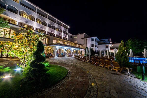 Un patio de hotel con pavimento de piedra, mobiliario exterior y zona de piscina.