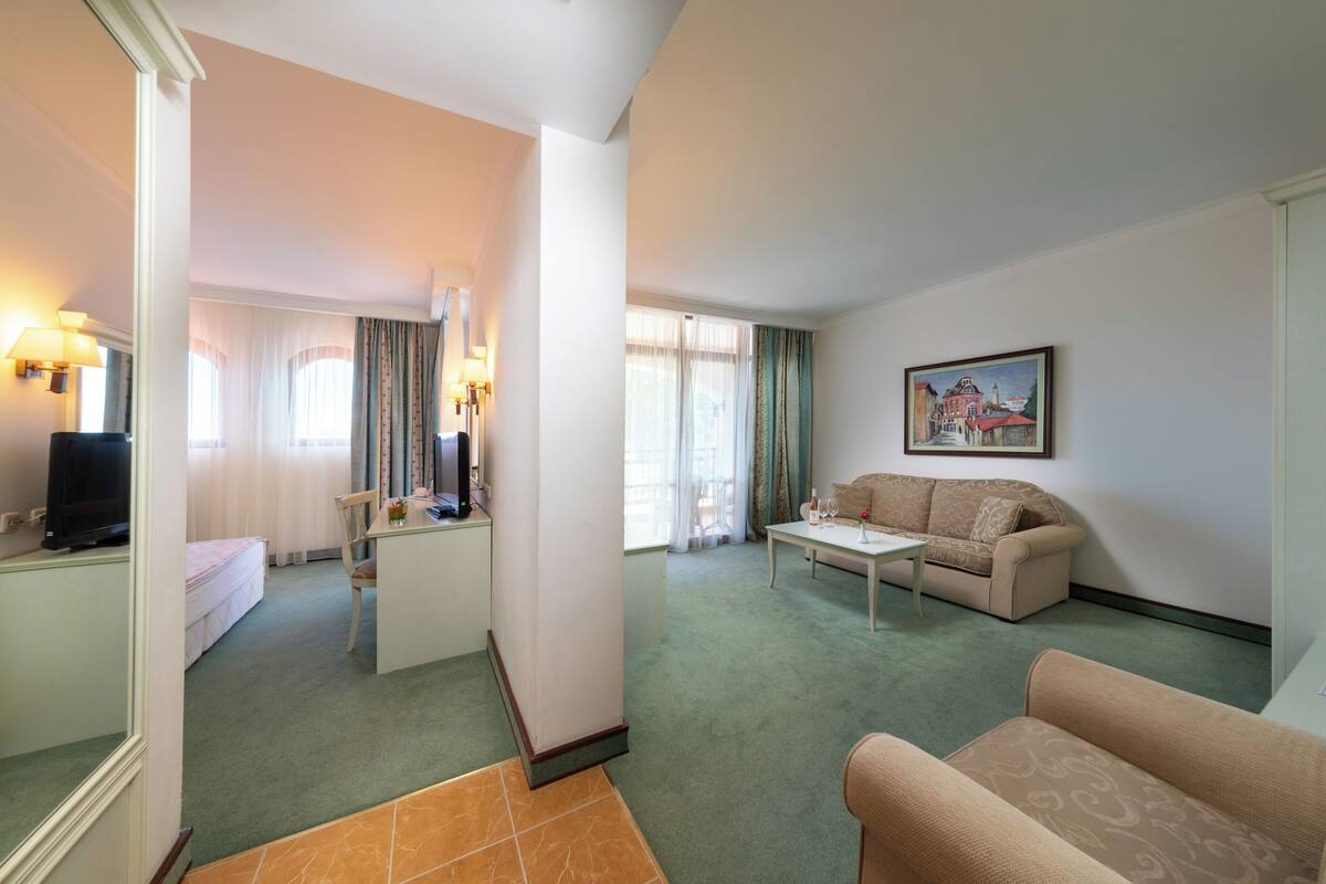 A hotel room with a living area, a dining area, and a bedroom.