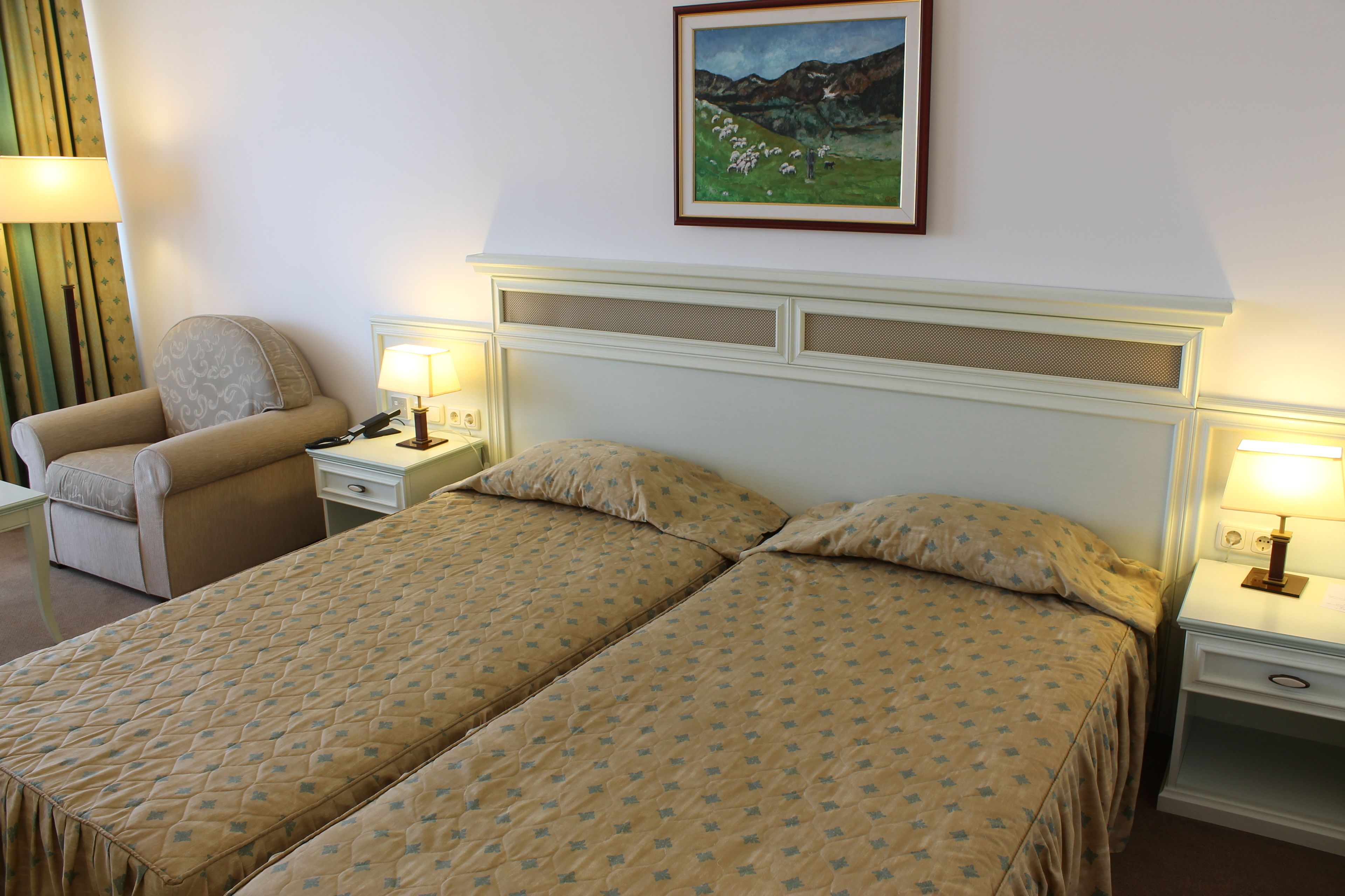 A hotel room with two beds, a chair, a nightstand, and a painting on the wall.