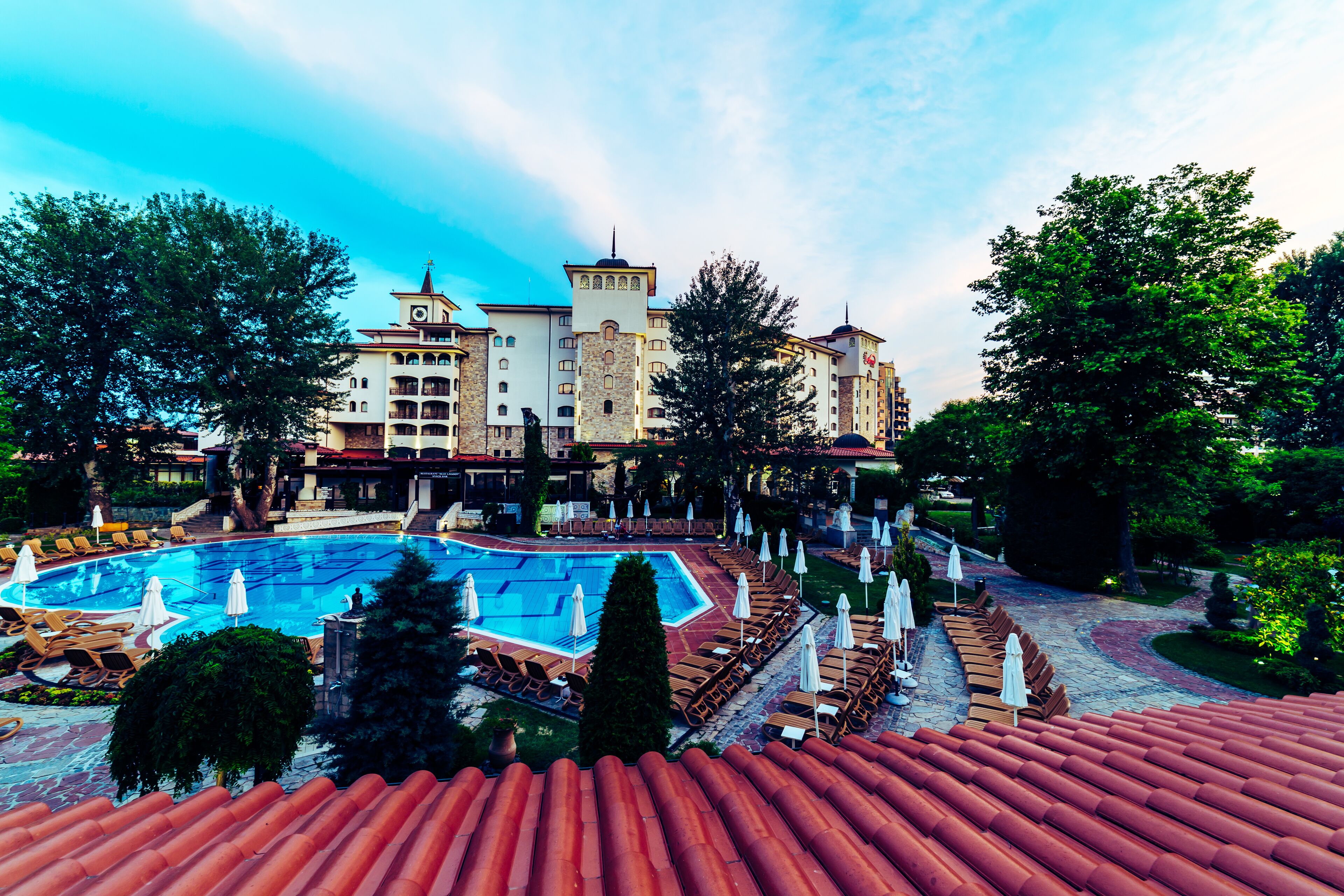 Un hôtel doté d’une piscine, de chaises longues et d’un toit recouvert de tuiles rouges.