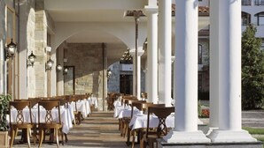A covered outdoor dining area with rows of tables and chairs, stone walls, and columns. - Helena VIP Villas and Suites (Sunny Beach)
