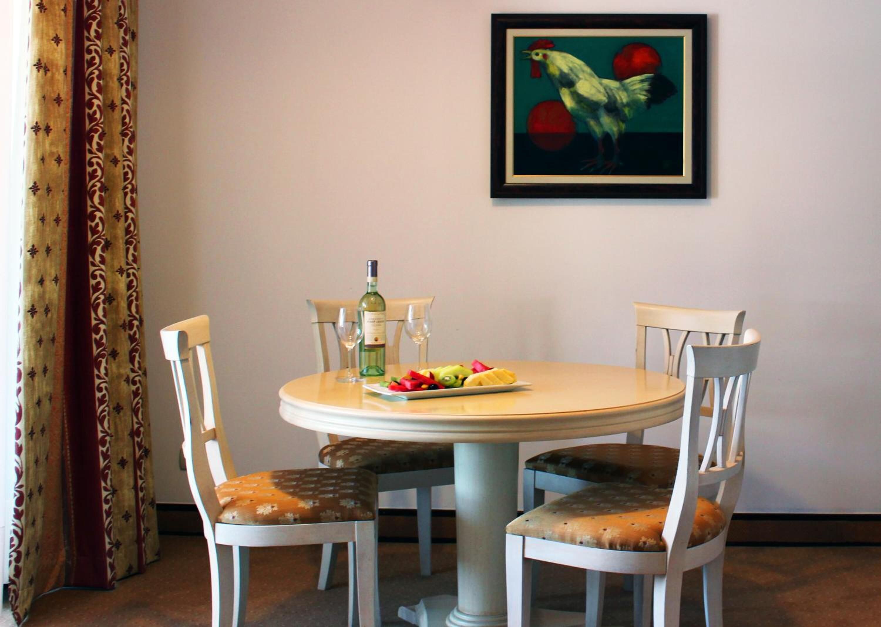 A dining area with a round table, four chairs, a bottle of wine, and a plate of fruit.