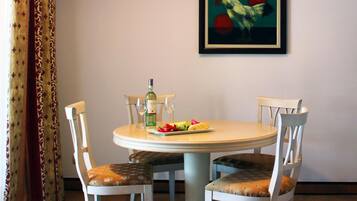 A dining area with a round table, four chairs, a bottle of wine, and a plate of fruit.