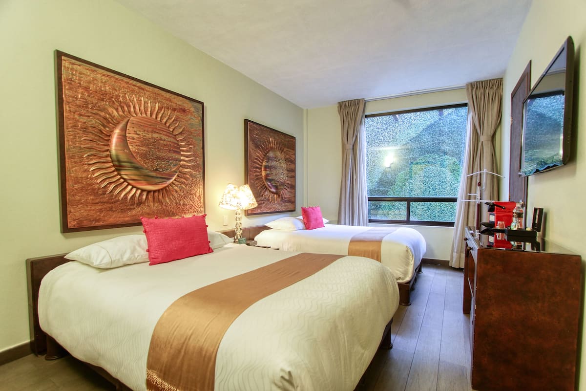 Quarto de hotel com duas camas, uma janela grande e obras de arte nas paredes.