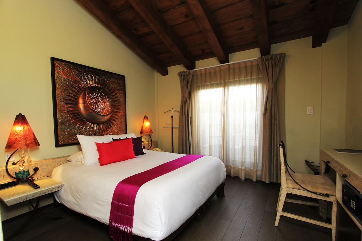 Quarto de hotel com uma cama grande, duas luminárias de cabeceira, uma escrivaninha e uma cadeira.
