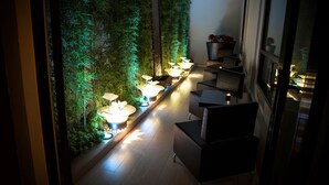 A narrow corridor with a vertical garden wall, illuminated by soft lighting, and furnished with modern seating.