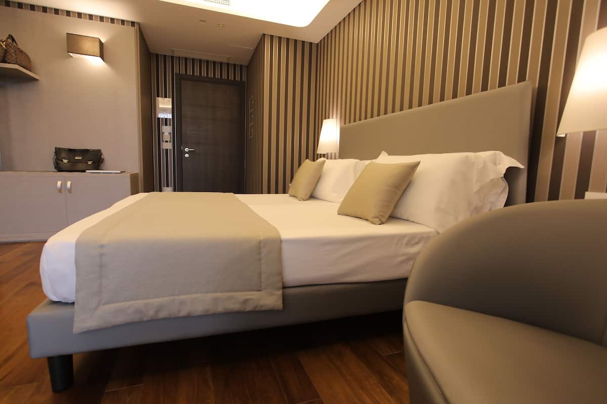 Ein modernes Hotelzimmer mit einem großen Bett, Nachttischlampen, einem Kleiderschrank und Holzböden.
