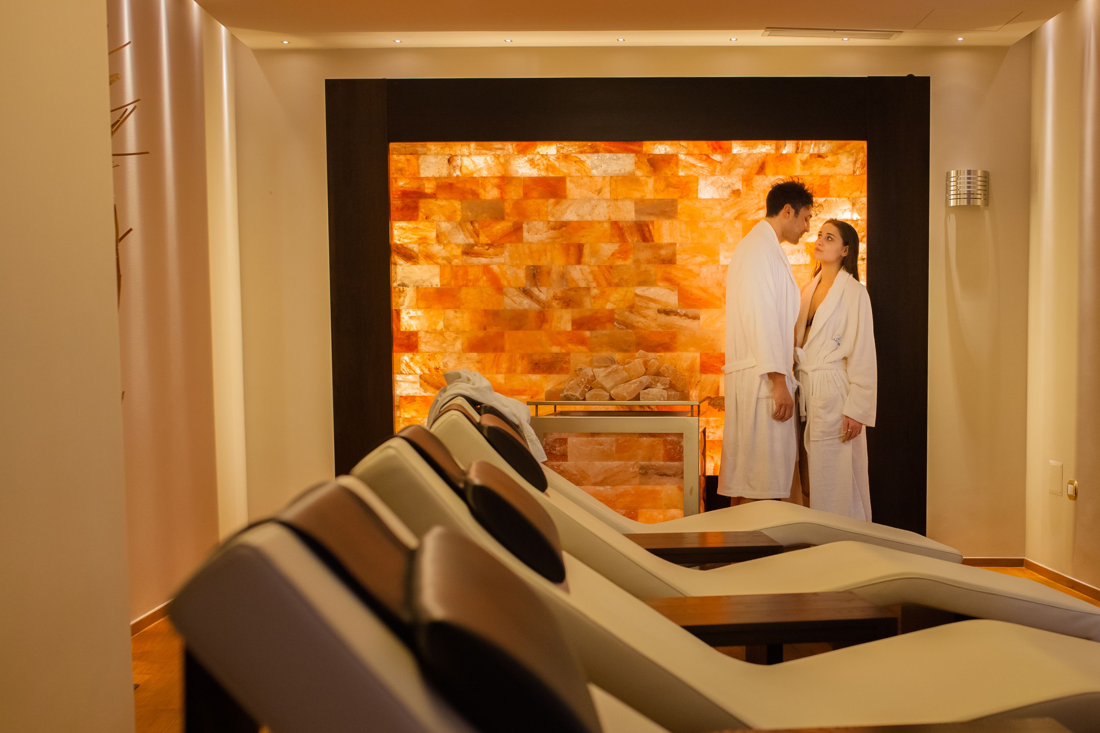 Un cuarto de spa con sillones de masaje, una pared de piedra y una camilla de masaje.