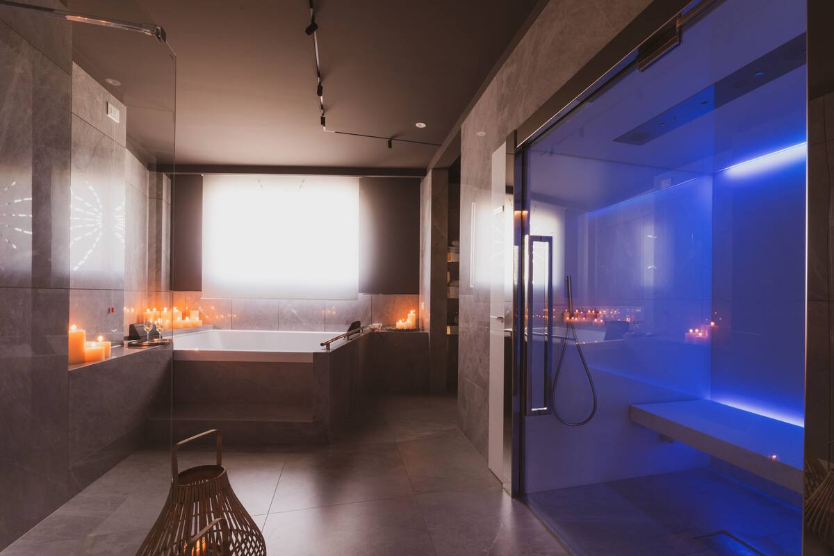 Ein modernes Badezimmer mit einer großen Badewanne, einer Duschkabine mit blauer Beleuchtung und Kerzen auf dem Waschtisch.