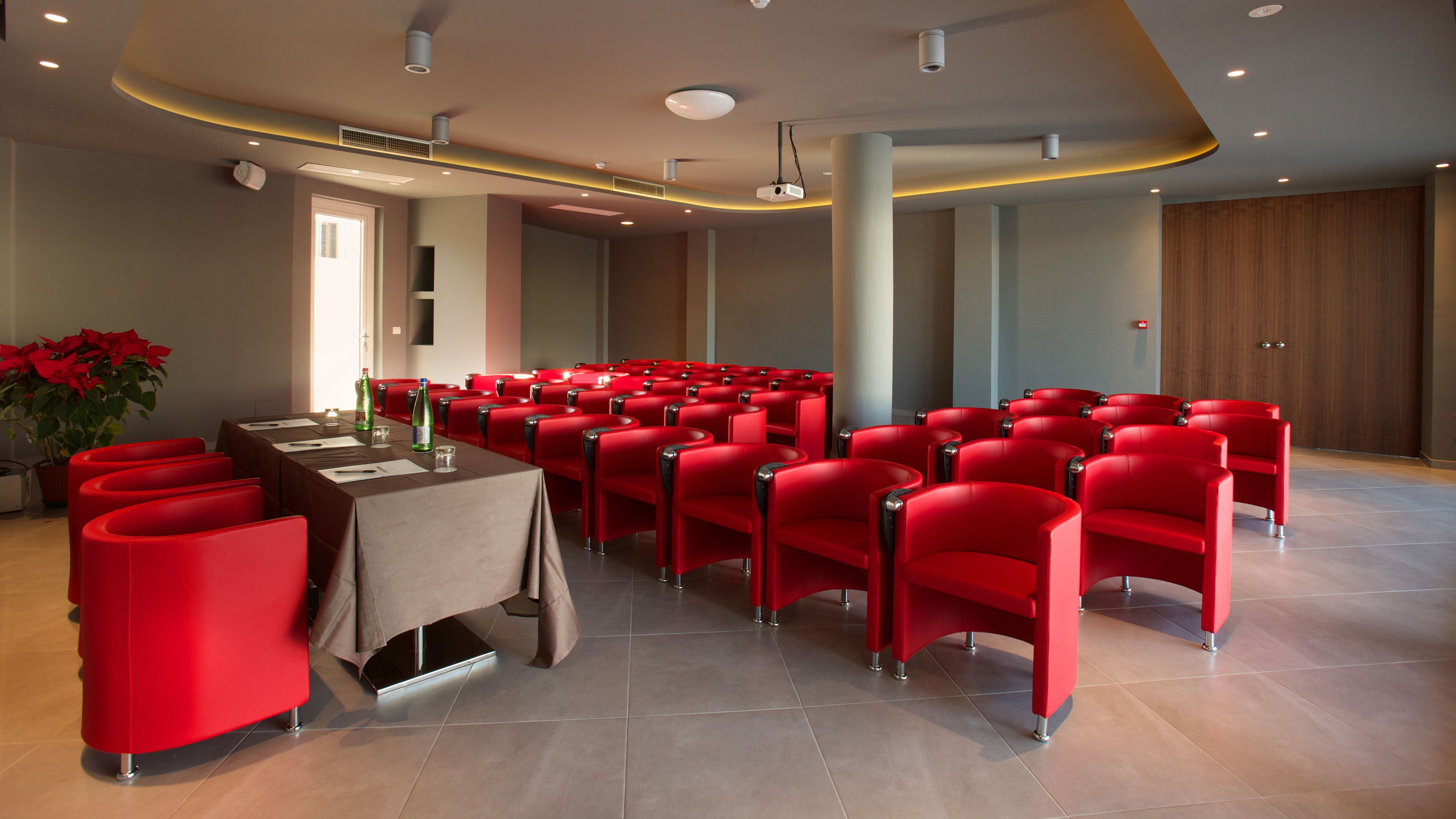 A conference room with red chairs, a table with a tablecloth, and a potted plant.