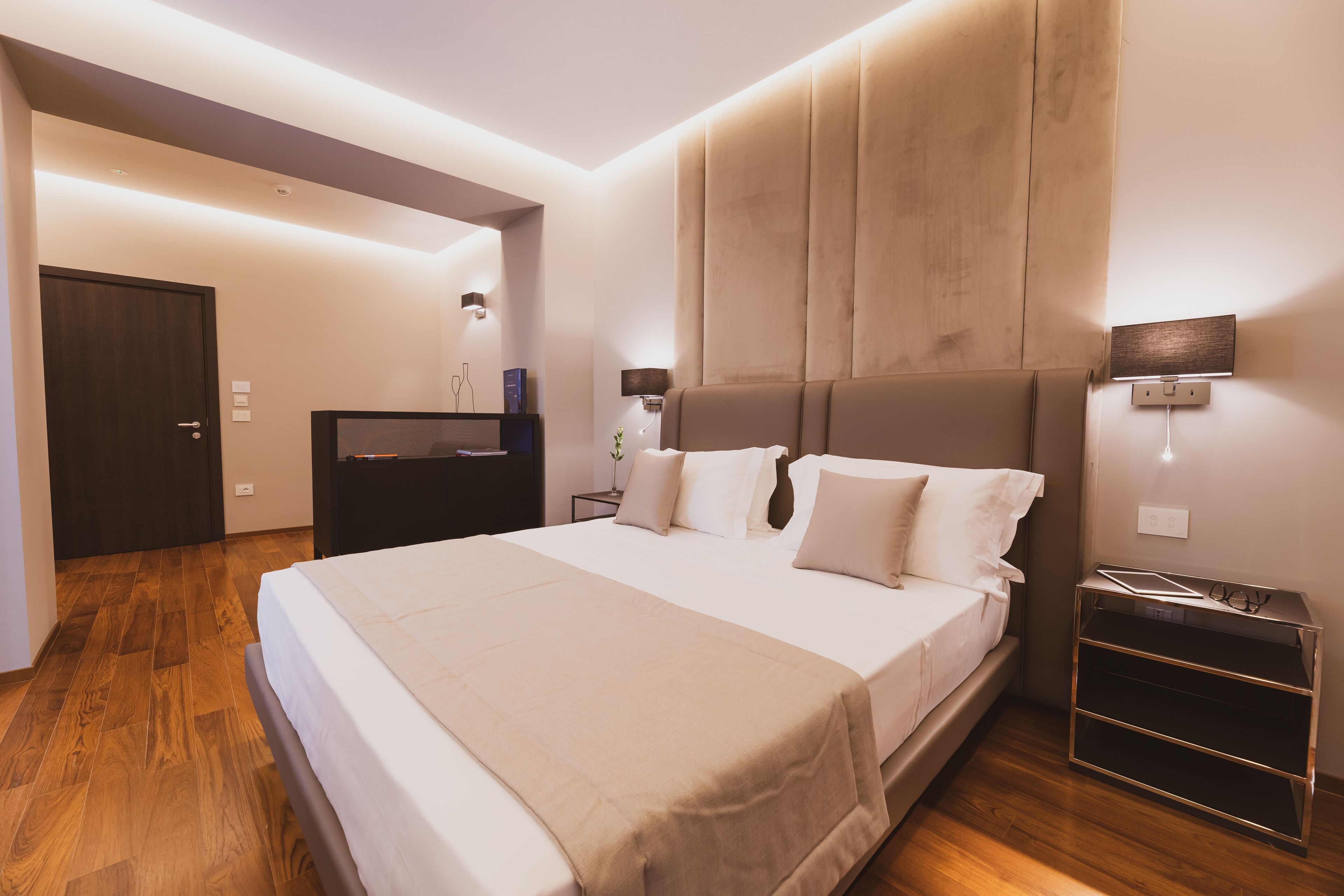 A modern bedroom with a large bed, bedside tables, a wardrobe, and a mirror.