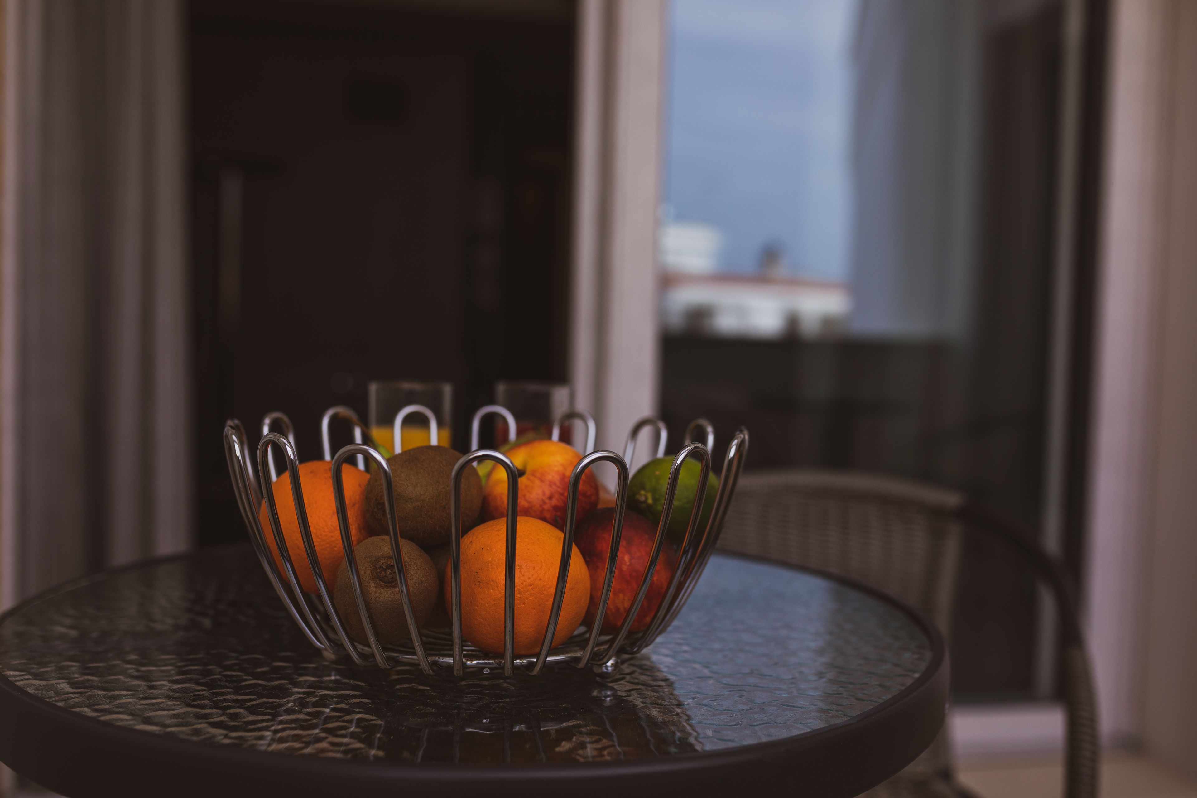 A round table with a metal fruit holder containing oranges and apples.