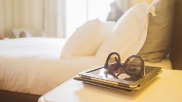A neatly made bed with white and brown pillows, a tablet with glasses on top, and a bedside table.