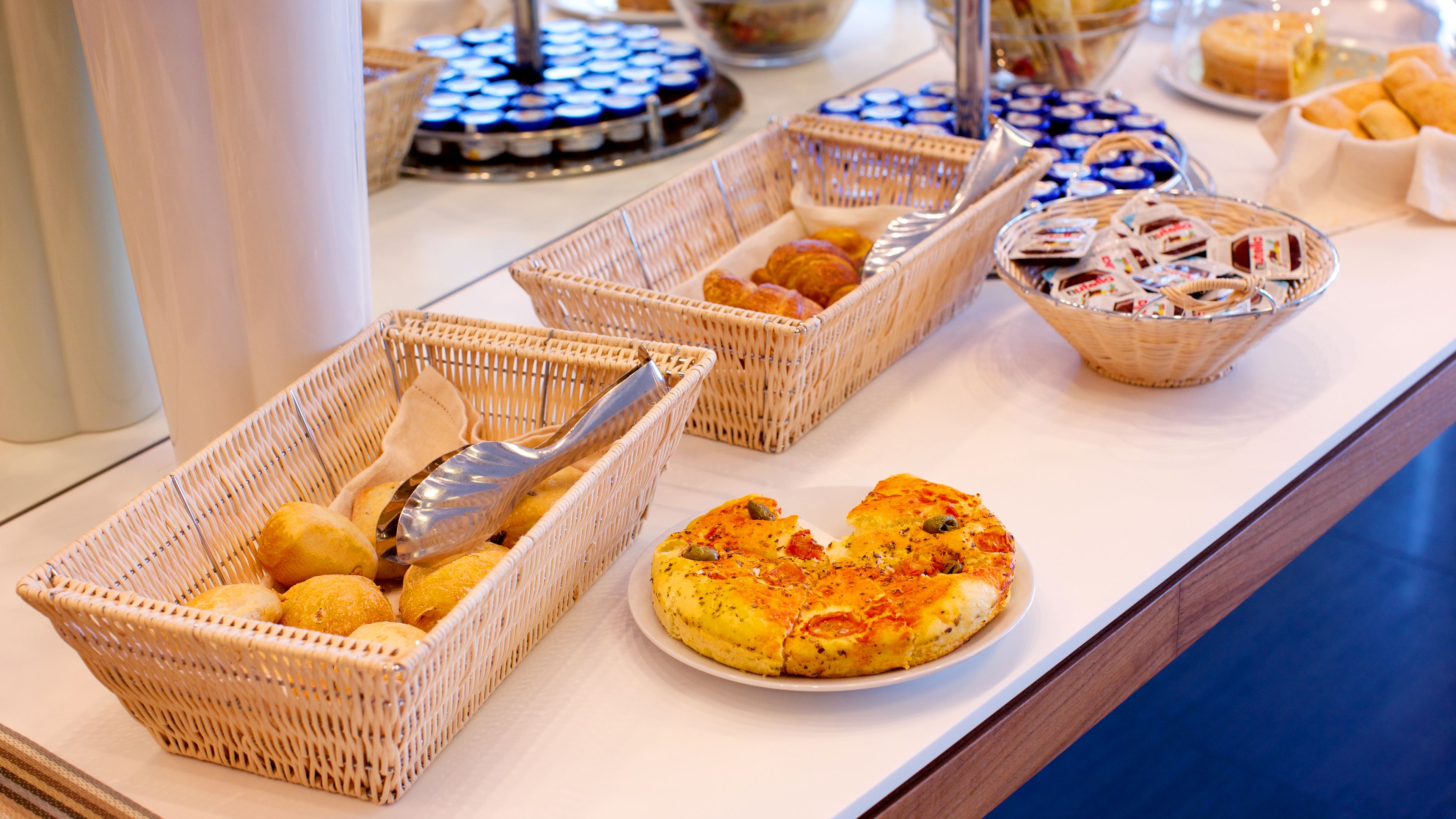 Una mesa de buffet con diversos alimentos en cestas de mimbre, incluyendo pan, pasteles y una bandeja de productos horneados.
