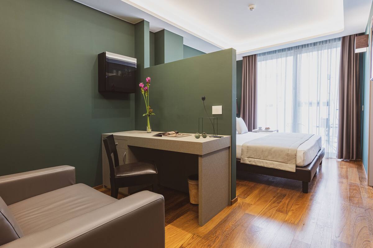 Ein Hotelzimmer mit Bett, Schreibtisch, Stuhl, Fernseher und einem Fenster mit Vorhängen.