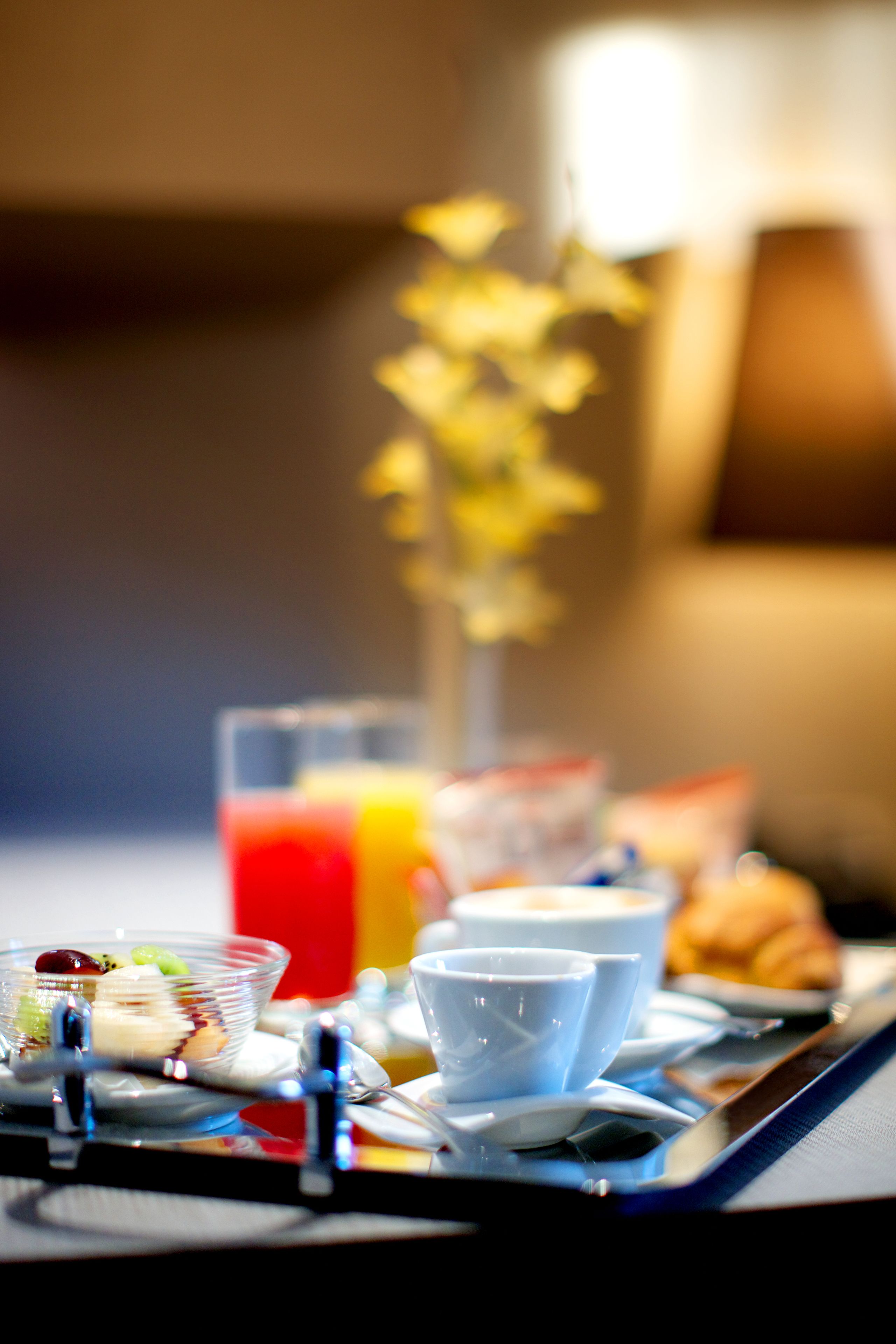 A breakfast tray with a glass of orange juice, a bowl of fruit, a croissant, and a cup.