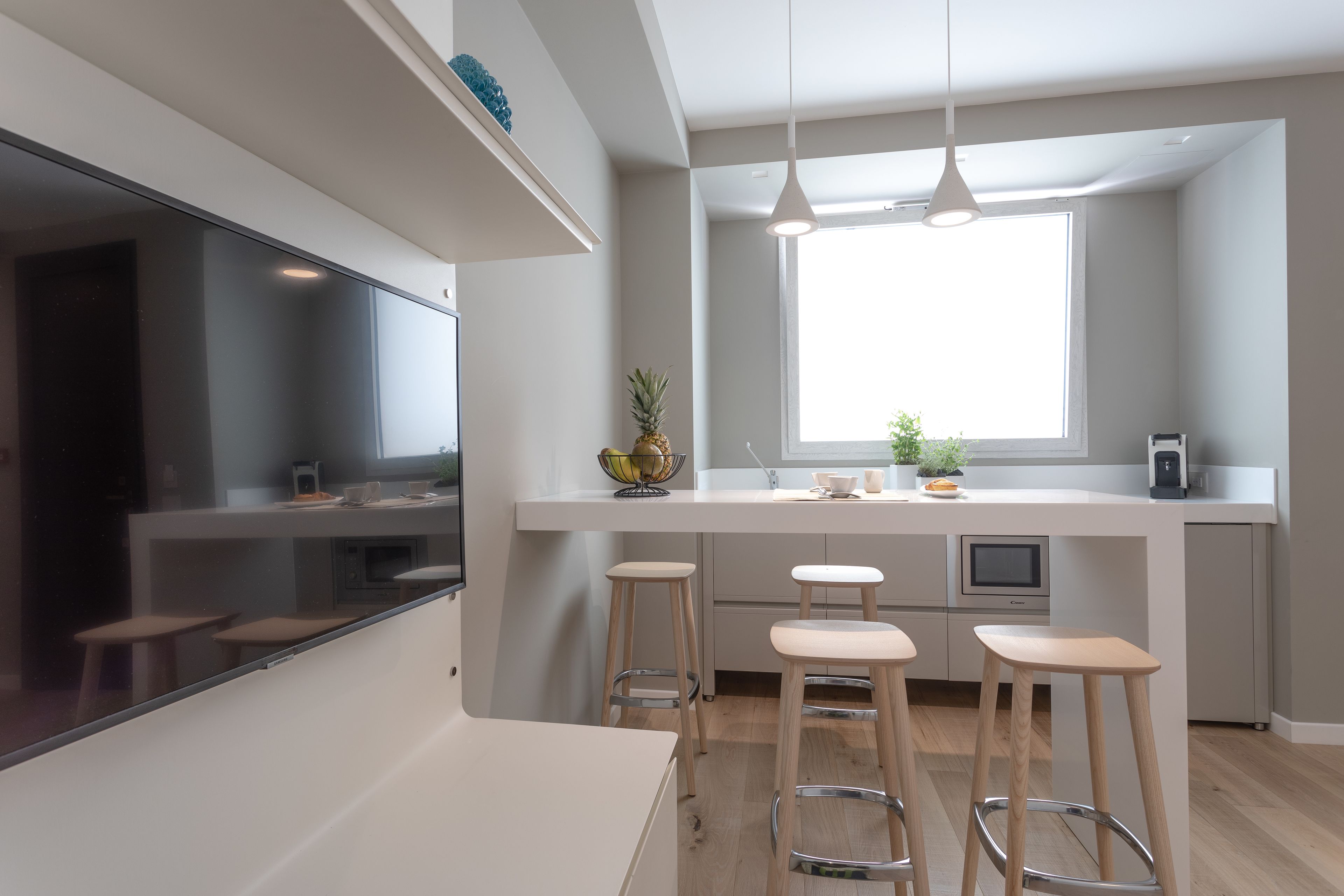 A modern kitchen with a large window, wooden stools, and a white countertop.