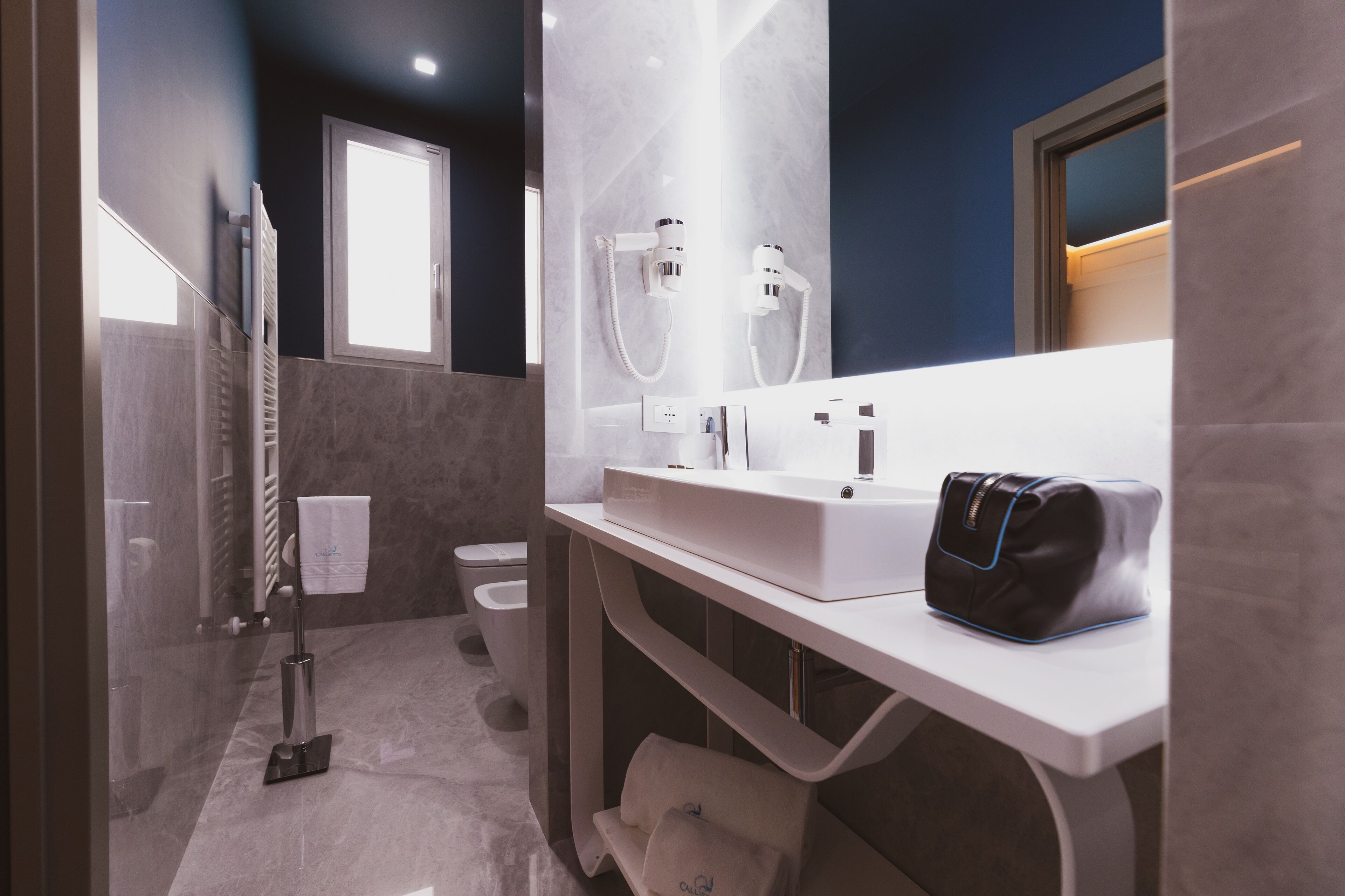A modern bathroom with a glass-enclosed shower, a white vanity with a black bag, and a toilet.