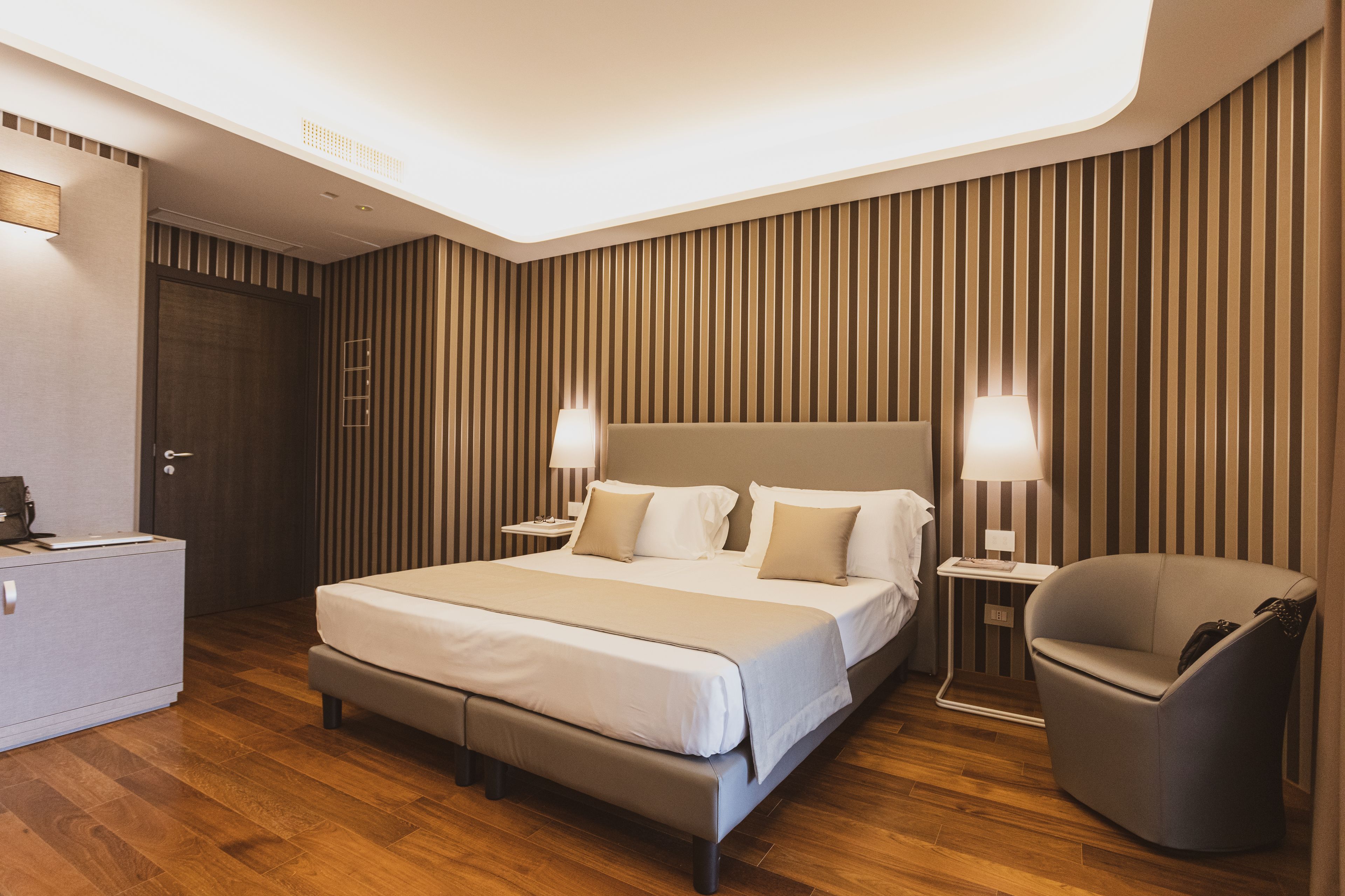 Une chambre d’hôtel moderne avec un grand lit, des tables de chevet avec des lampes, un coin salon et une armoire.