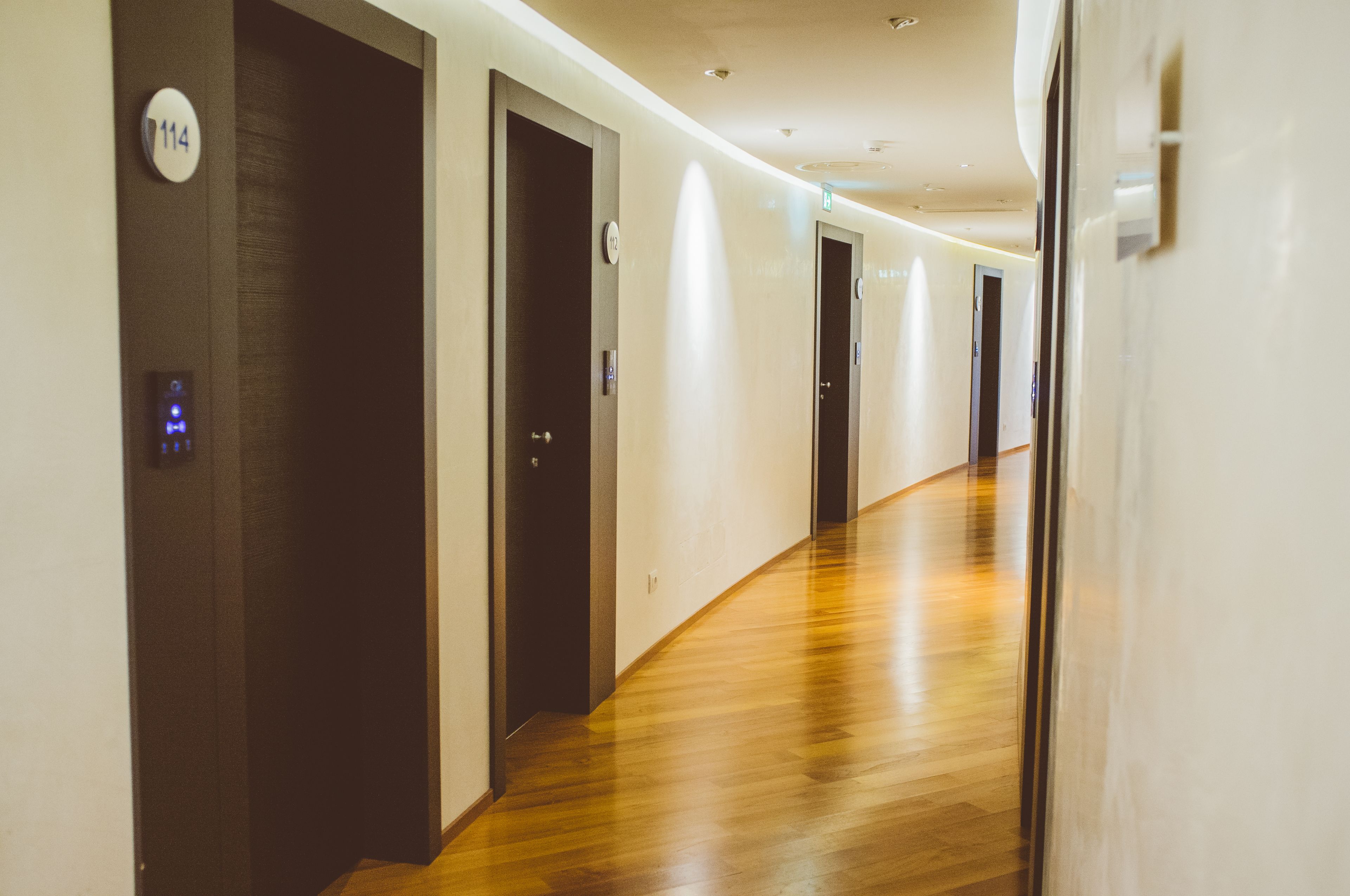 Pasillo de hotel con suelo de madera, puertas y un letrero que indica la habitación 114.
