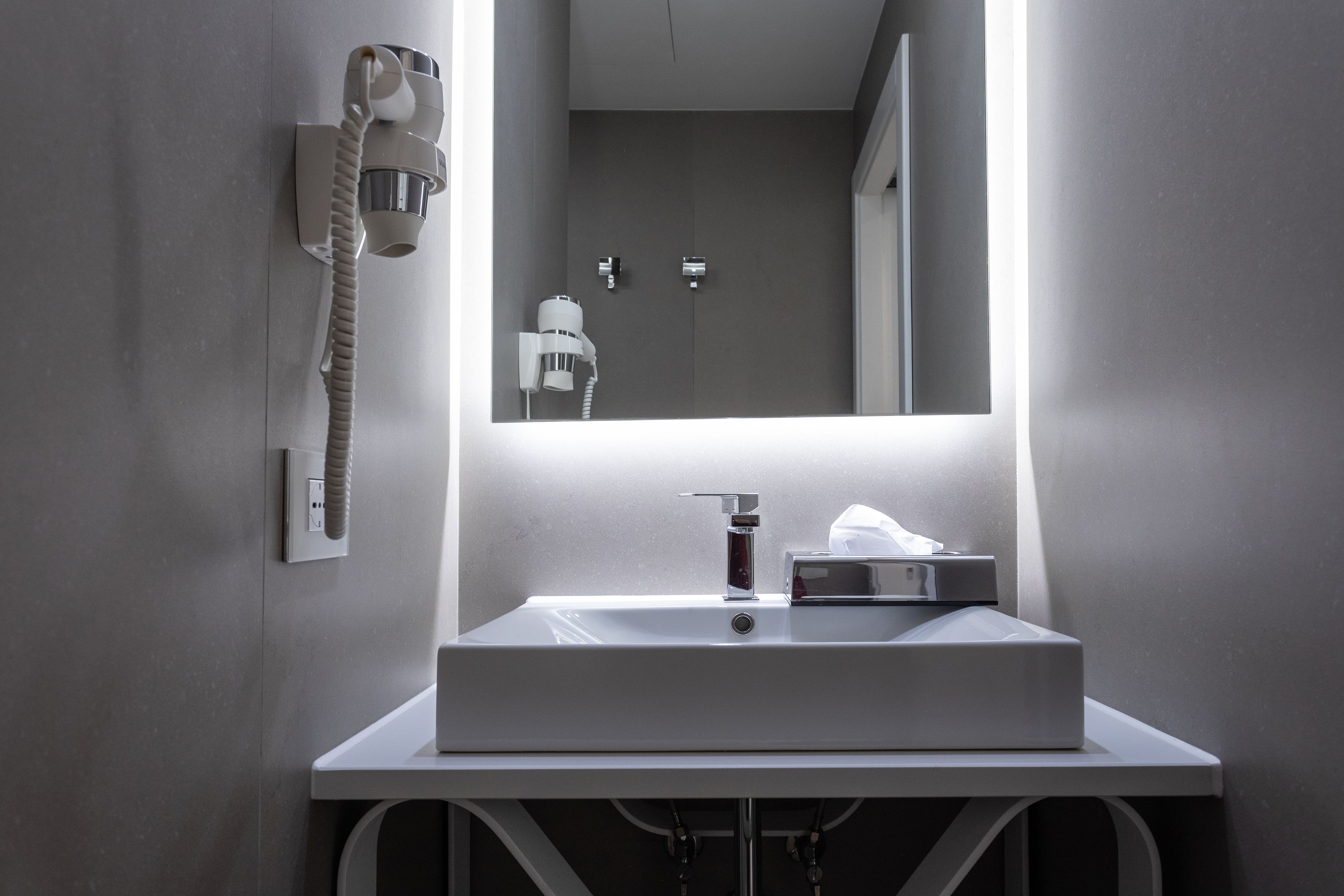 A modern bathroom with a white sink, a mirror, and a hairdryer mounted on the wall.