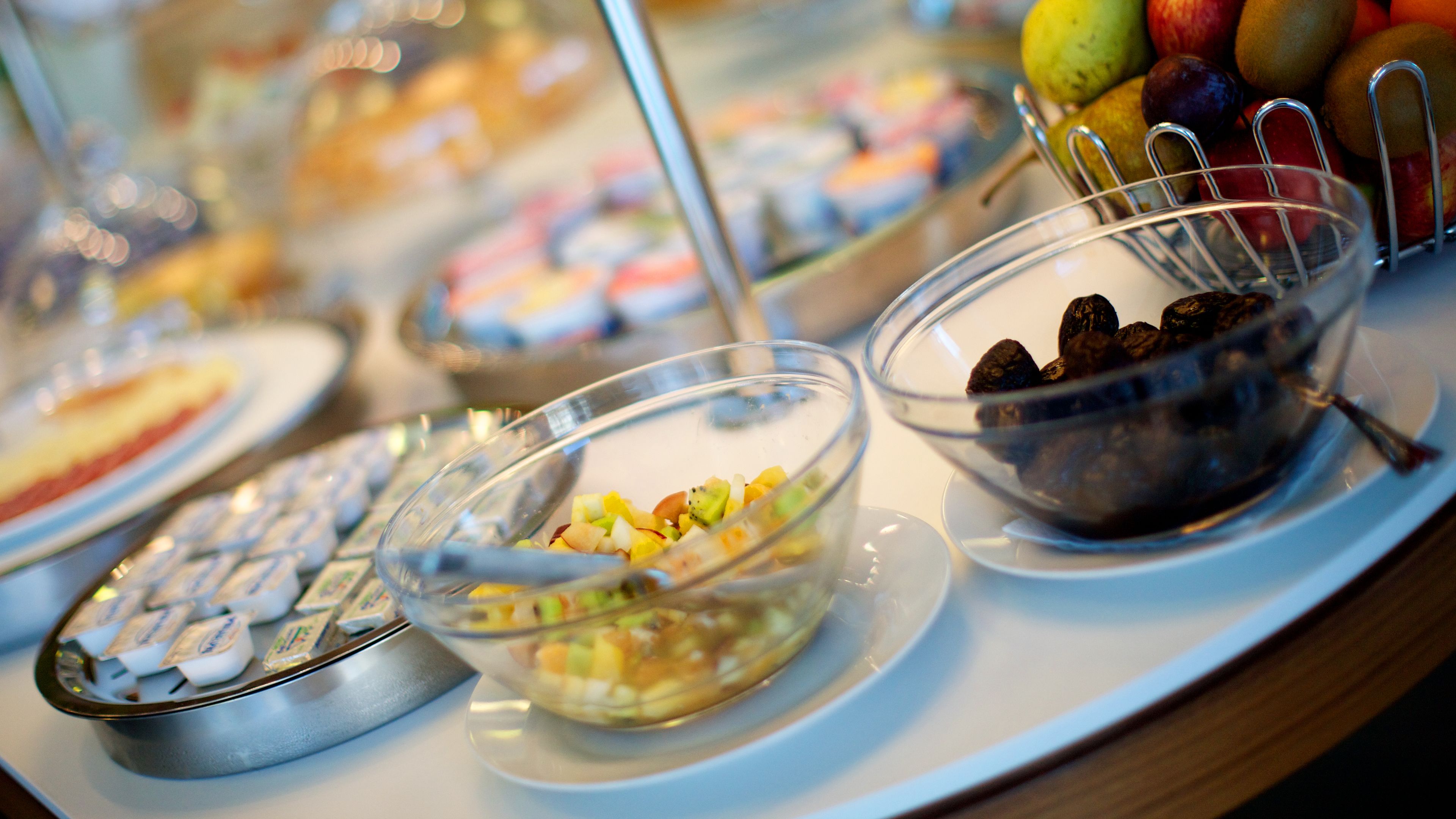 Une table de buffet proposant divers aliments, notamment des fruits, des noix et un bol de yaourt aux fruits et au granola.