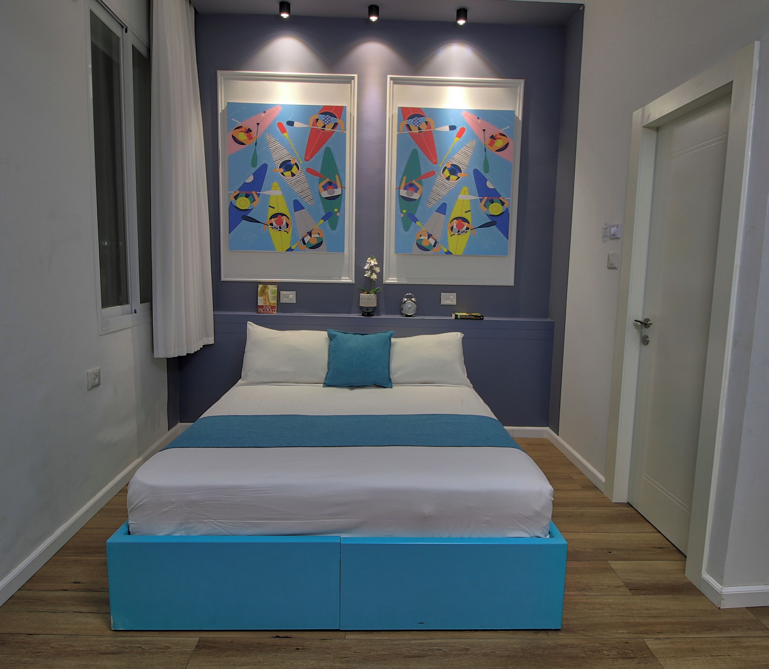 A bedroom with a bed, two paintings, a clock, and a small potted plant.