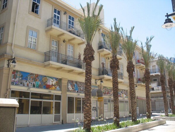 A multi-story building with balconies, palm trees, and a mural on the ground floor. - 1926 Designed Apartments Hotel (Haifa)