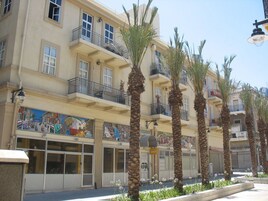 Un edificio de varios pisos con balcones, palmeras y un mural en la planta baja.