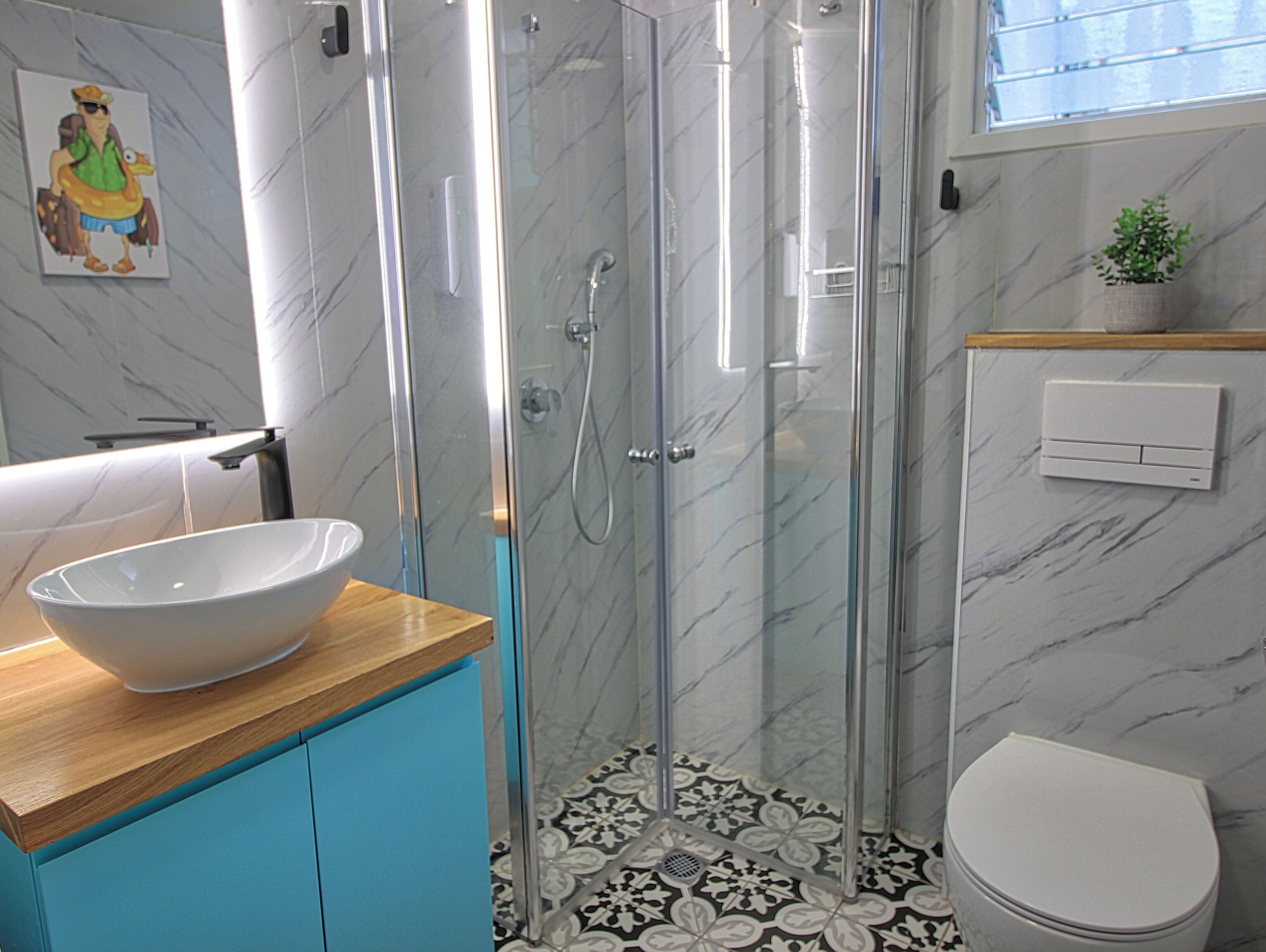 A bathroom with a glass-enclosed shower, a white sink, a toilet, and a decorative tile floor.