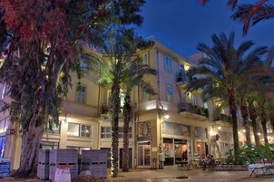Un hotel de varios pisos con balcones, palmeras y zonas de estar al aire libre.