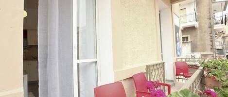 A balcony with red chairs, a white curtain, and potted plants.