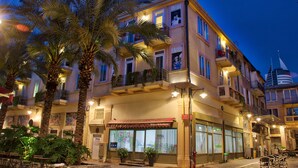 Ein mehrstöckiges Hotel mit Balkonen, Palmen und einem Restaurant mit roter Markise.
