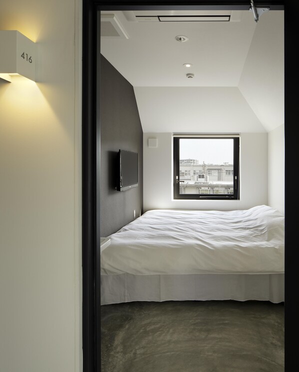 A modern hotel room with a large bed, a TV mounted on the wall, and a window providing a city view. - Piece Hostel Kyoto (Kyoto)