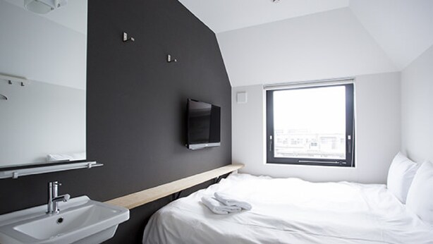 A modern hotel room with a large bed, a built-in TV, a window with a city view, and a sink with a mirror. - Piece Hostel Kyoto (Kyoto)