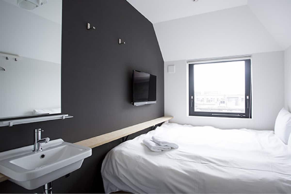 A modern hotel room with a large bed, a built-in TV, a window with a city view, and a sink with a mirror.